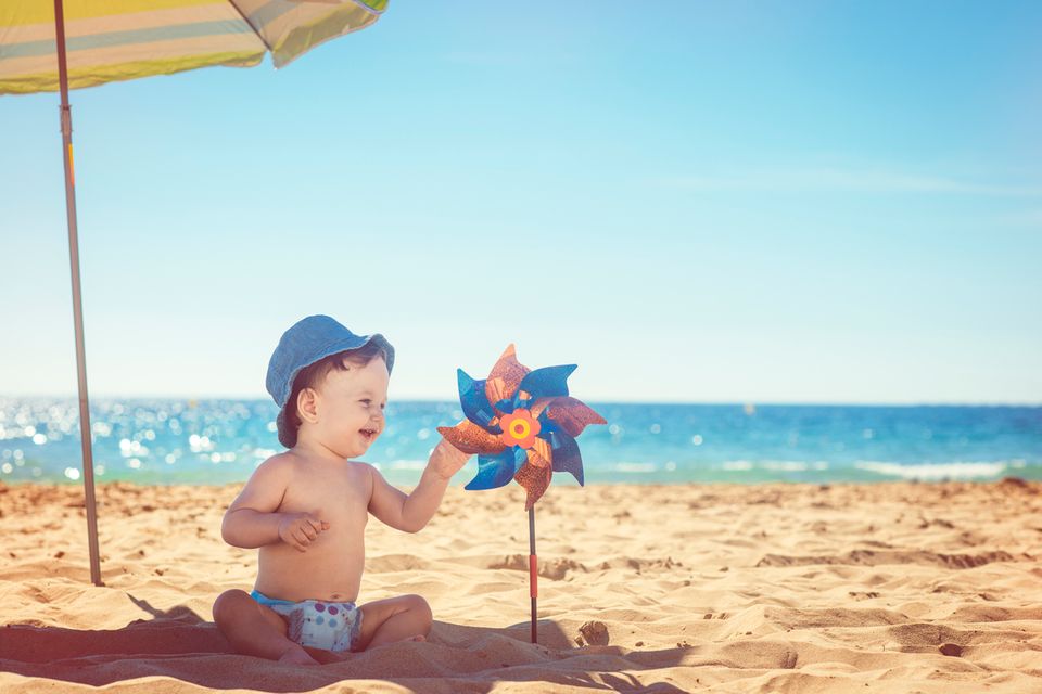 Baby-sitzt-unter-Sonnenschirm-am-Strand