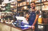 Lachender Verkäufer steht hinter der Kasse