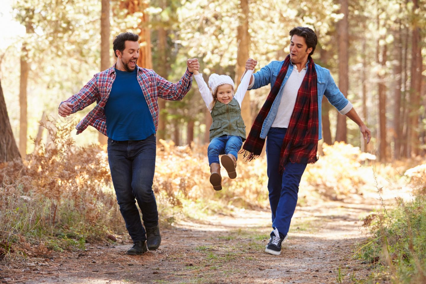 Zwei Väter laufen durch den Wald, halten die Tochter an den Händen zwischen sich