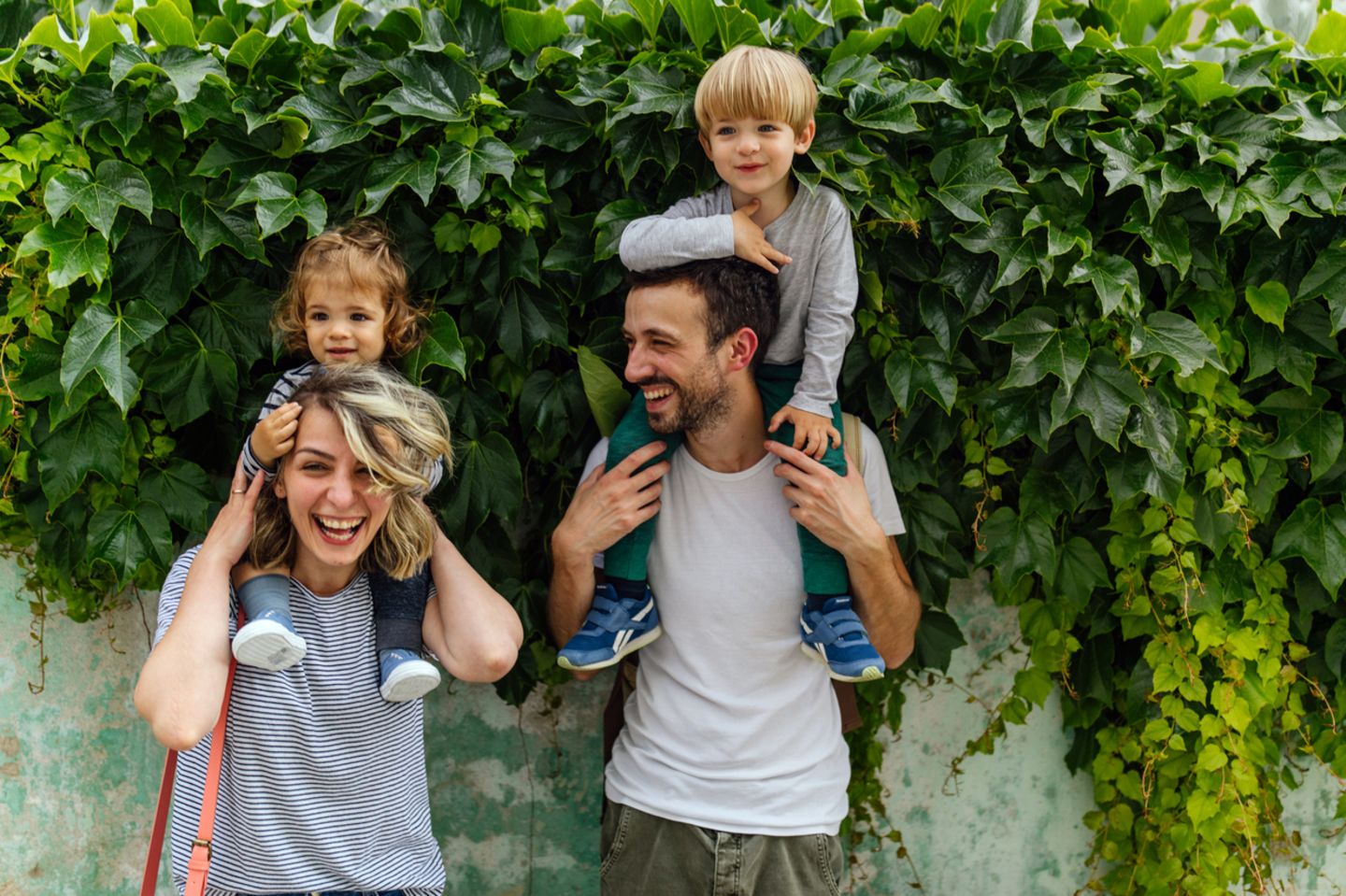 Familie steht vor einer Mauer mit Efeu und lachen