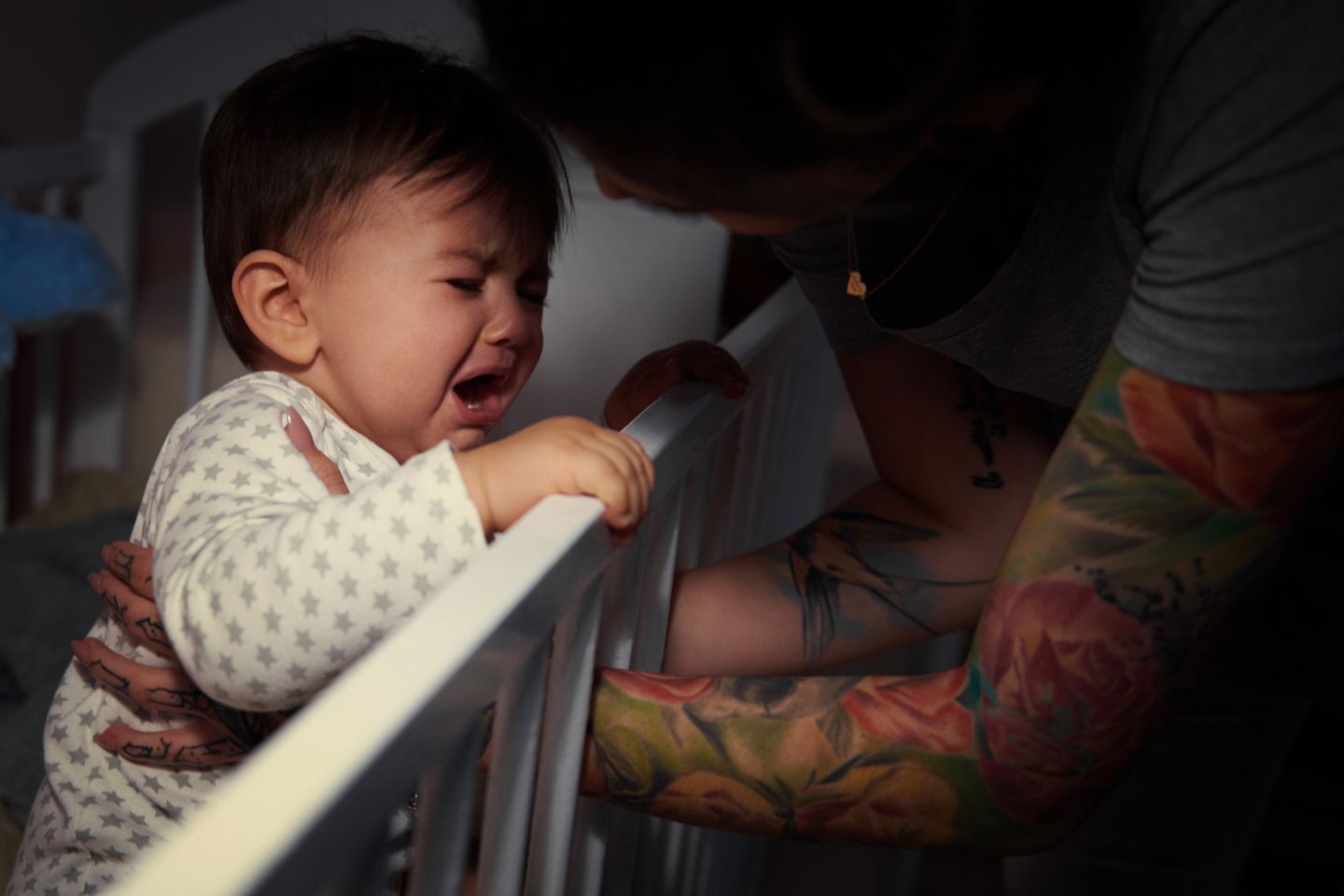 Frau holt schreiendes Baby aus dem Gitterbett