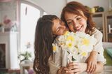 Tochter umarmt Mutter und überreicht ihr Blumen