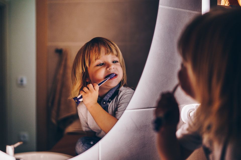 Kleiner Junge putzt sich vor dem Spiegel im Badezimmer die Zähne