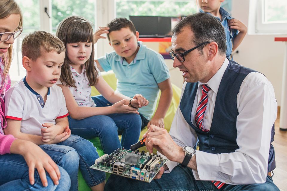 Betriebliche Kinderferienbetreuung, ein männlicher Lehrer unterrichtet Grundschulkinder in Computertechnik