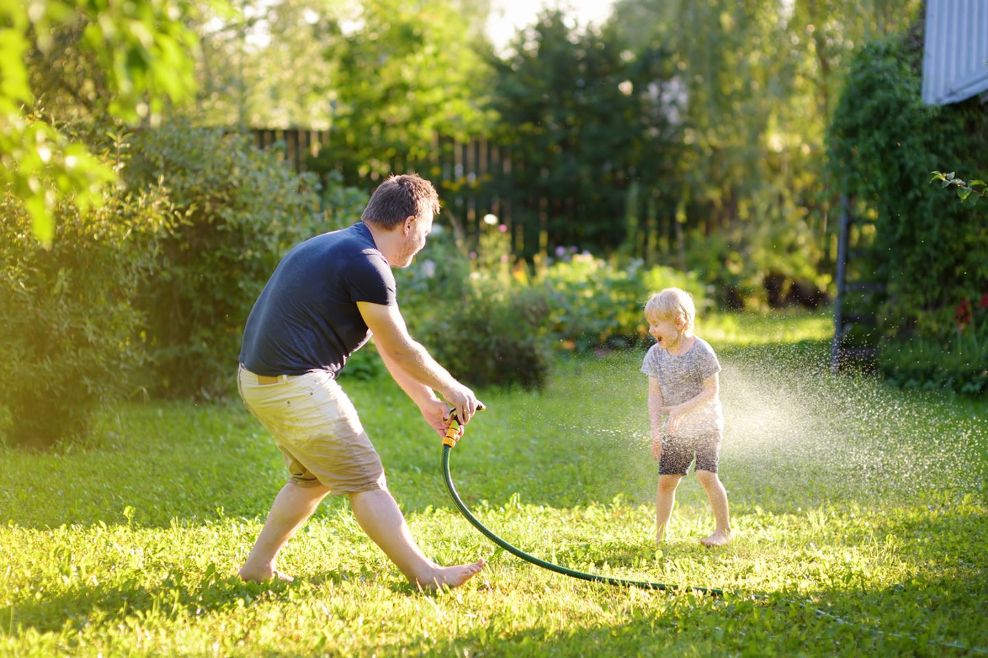 Vater und Kind spielen mit Gartenschlauch
