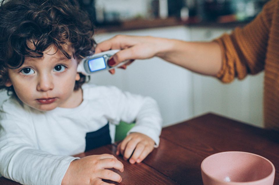 Fieber messen: Einem Kind mit dunklen locken wird im Ohr Fieber gemessen