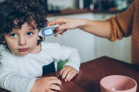 Fieber messen: Einem Kind mit dunklen locken wird im Ohr Fieber gemessen