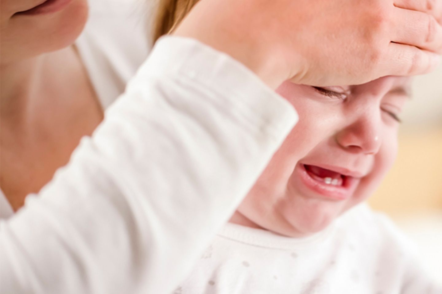Fieber messen: Frau legt einem weinenden Baby die Hand auf die Stirn