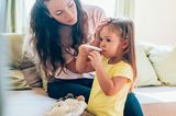 Fieber messen: Mutter achtet darauf, wie die kleine Tochter im Mund Fieber misst.