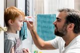 Fieber messen: Ein Vater hält seinem Sohn ein Fieberthermometer an die Stirn.