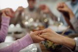 Familie hält sich am Esstisch an den Händen