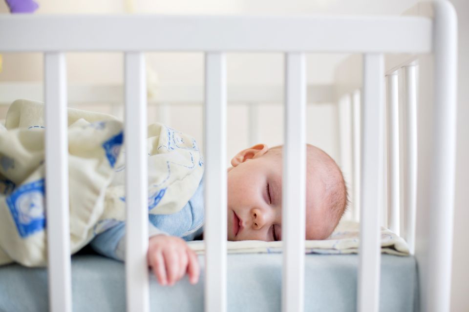 Baby liegt in seinem Gitterbettchen und schläft