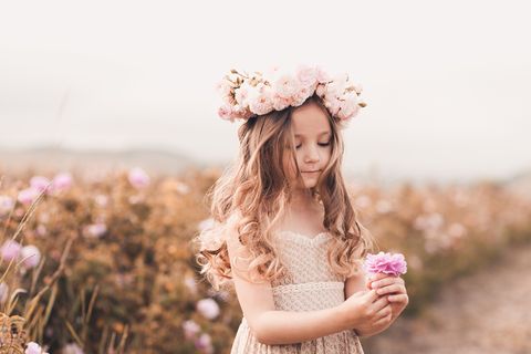 Mädchen mit Blumenkranz schaut auf eine gepflückte Blume