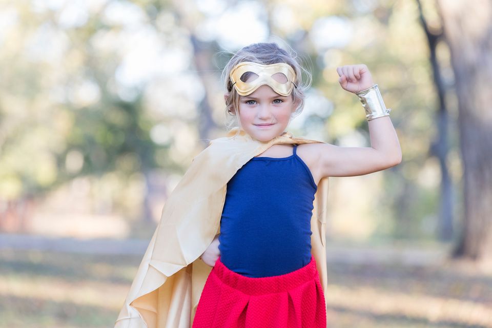Kleines Mädchen im Superheldenkostüm zeigt ihren Bizeps