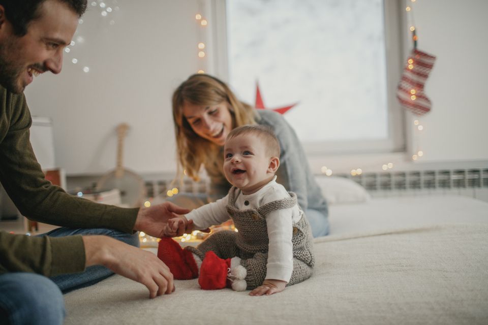 Weihnachtlich gekleidetes Baby sitzt auf dem Bett mit den Eltern
