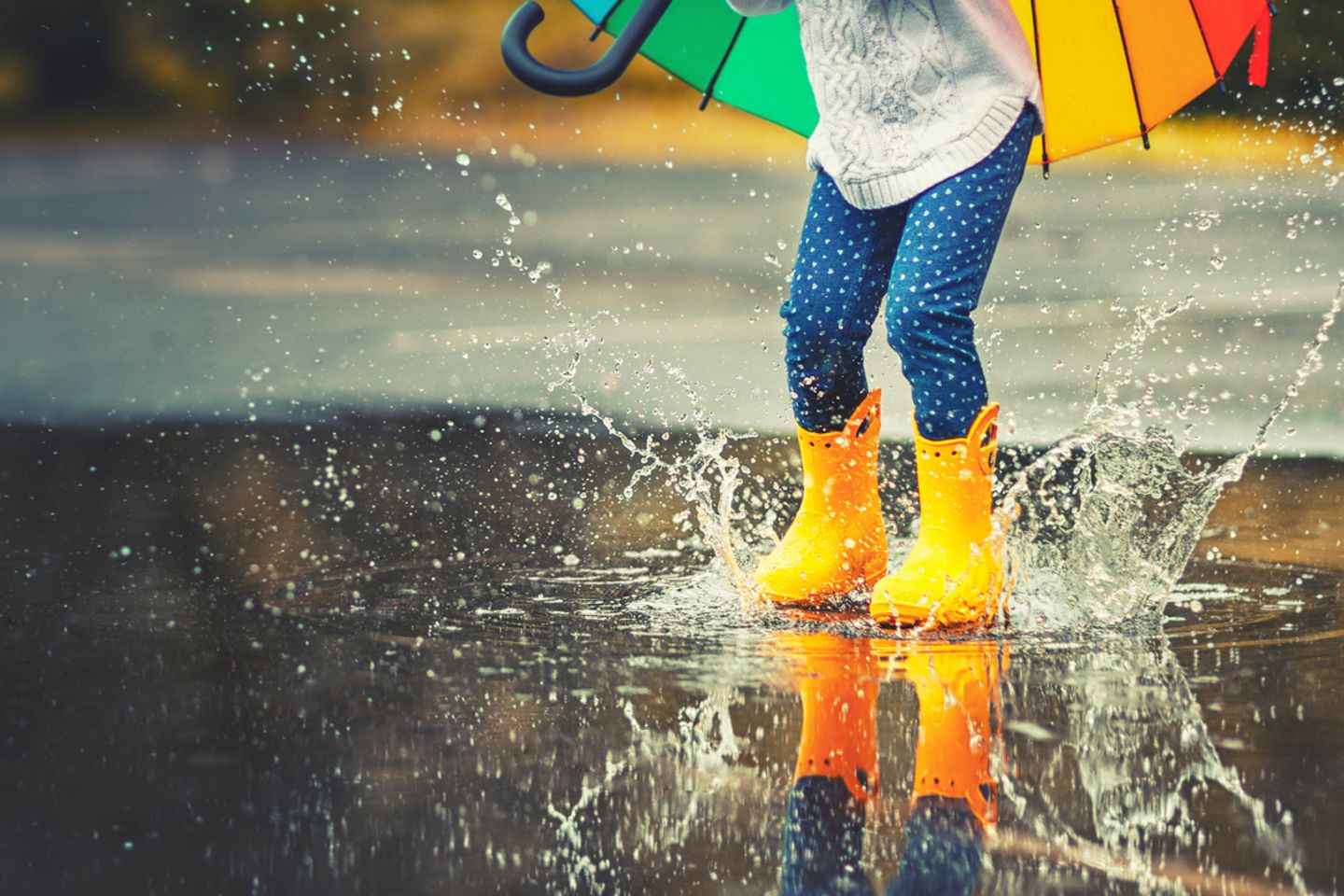 Füße eines Kindes in gelben Gummistiefeln springen in eine Pfütze im Regen