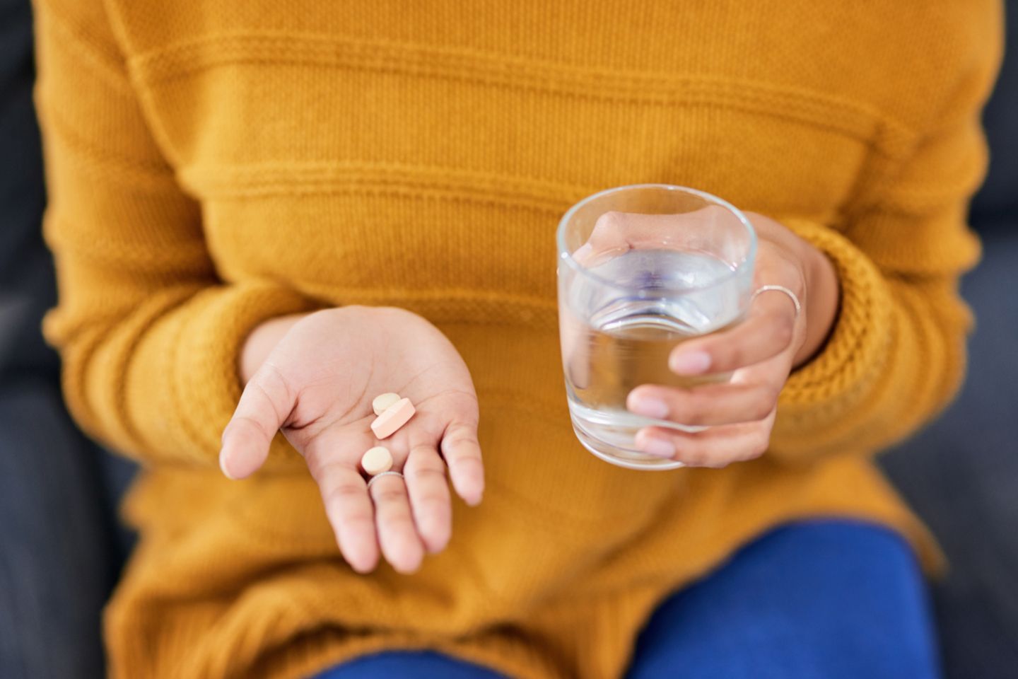 Frau mit gelbem Pullover, in einer Hand Tabletten