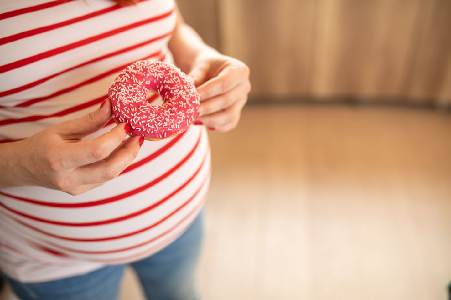 Schwangere Frau hlt einen Donut mit Zucker vor sich
