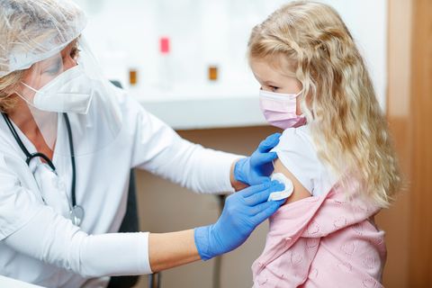 Ärztin impft kleines Mädchen mit Mundschutz