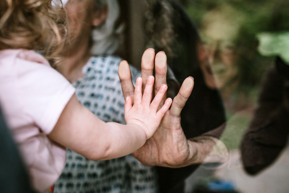 Ein kleines Mädchen presst von einer Seite mit der Hand gegen eine Fensterscheibe, die Großmutter von der anderen