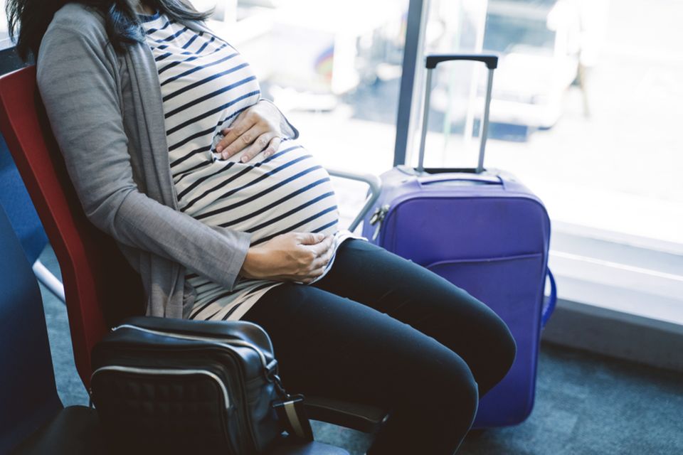 Schwangere sitzt am Flughafen und wartet auf das Flugzeug