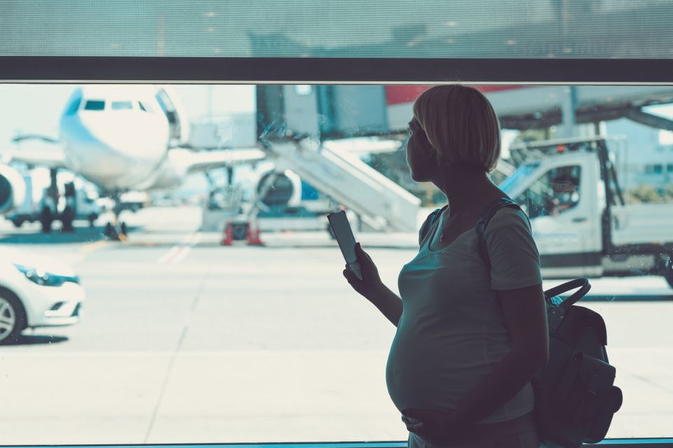 Schwangere steht am Fenster und schaut auf ein Flugzeug am Rollfeld