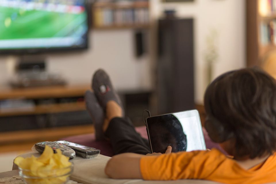 Junge sitzt vor dem Fernseher und isst Chips.