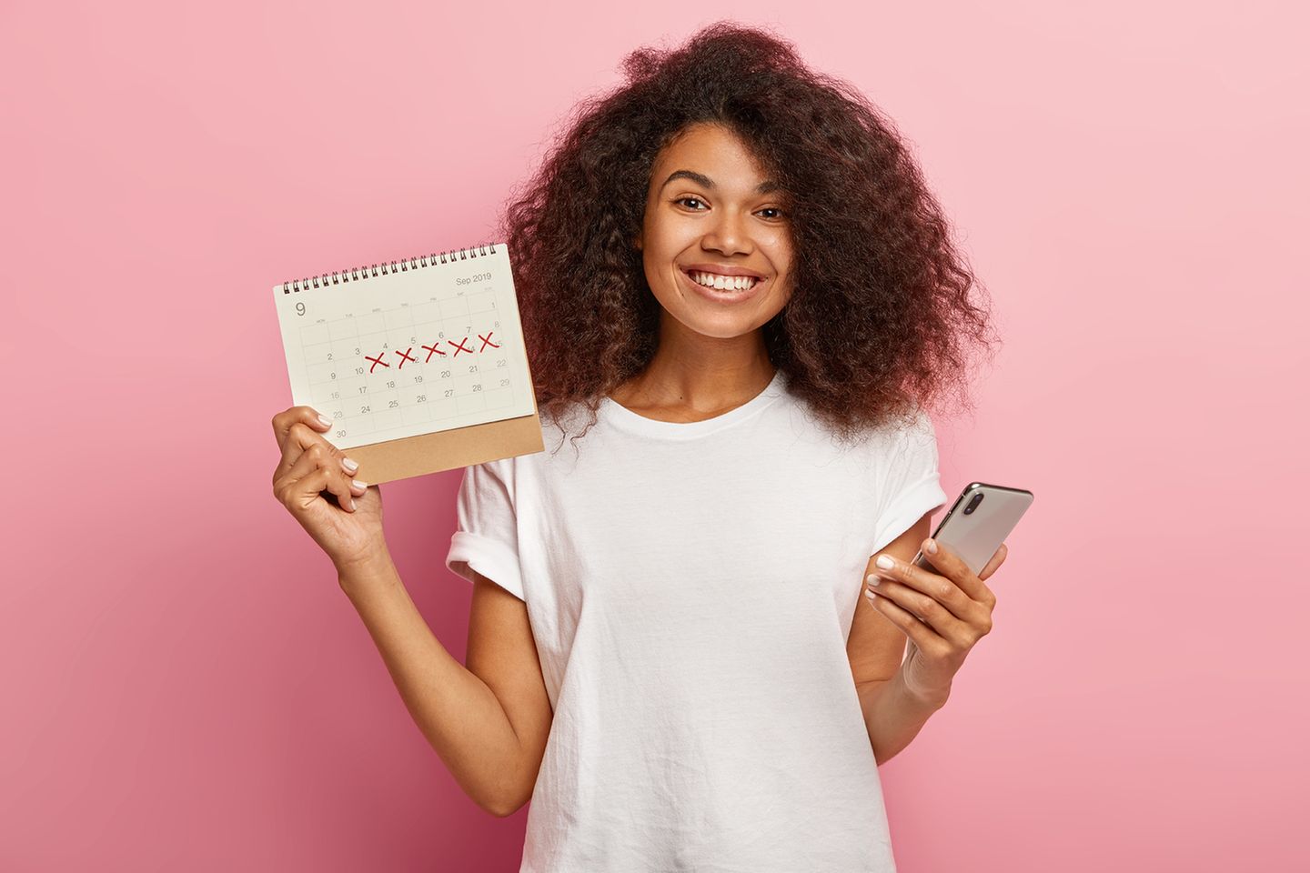 Eine glückliche Frau hält einen Periodenkalender und ihr Smartphone in die Kam