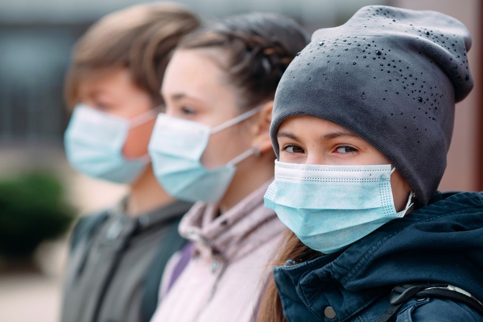 Drei Kinder stehen draußen mit Masken. Immer mehr Kinder erkranken nach einer COVID-19-Infektion an PIMS