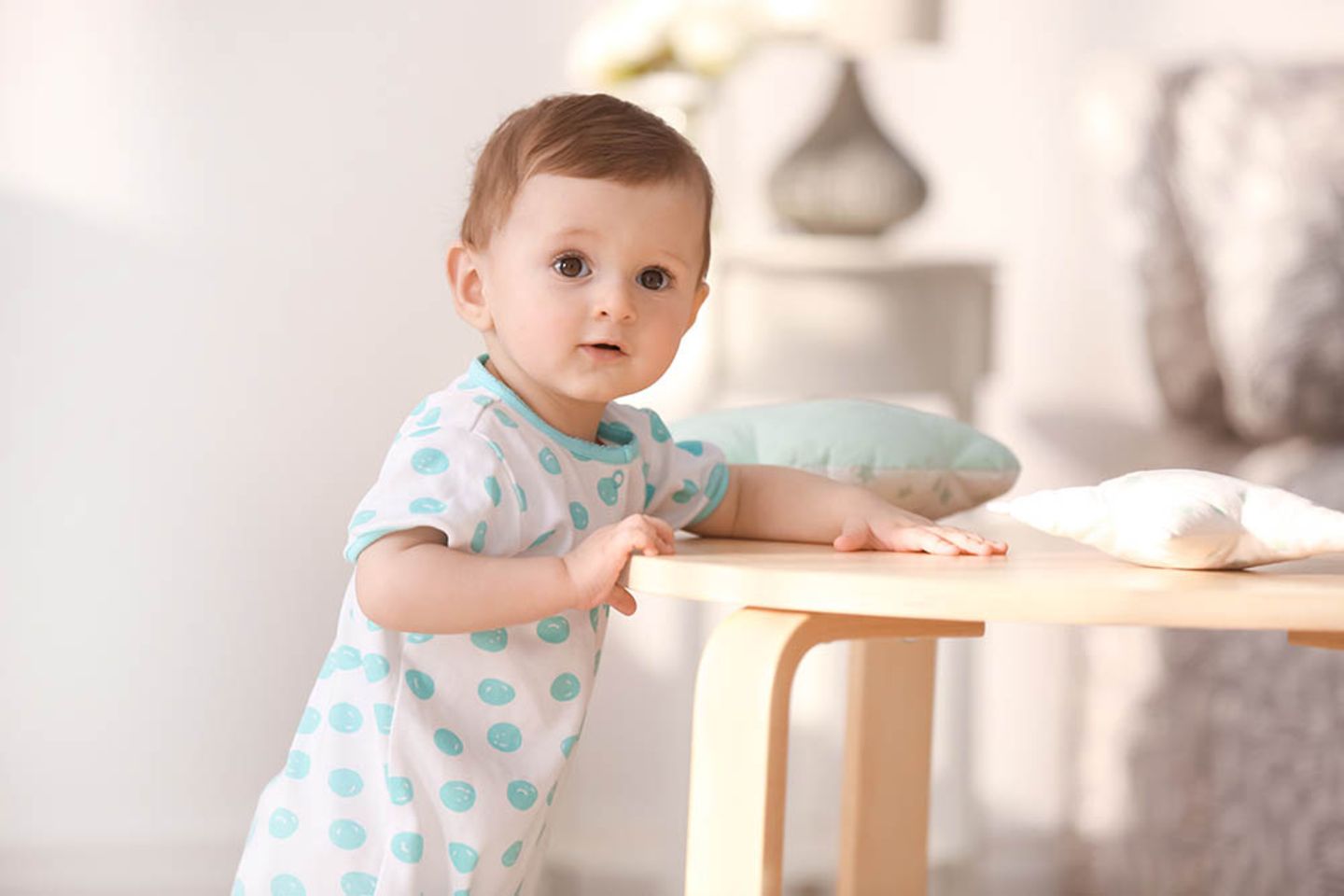 Baby 1 Jahr: Niedliches Kleinkind steht an einem kleinen Tisch