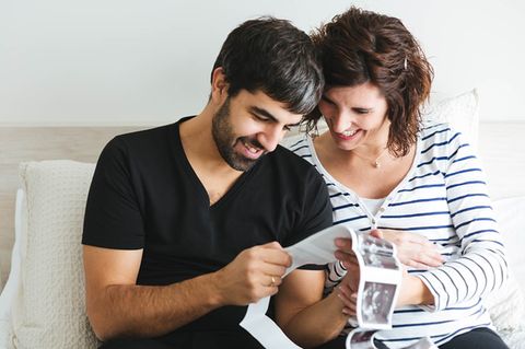 Schwangeres Paar schaut glücklich Ultraschallbilder an