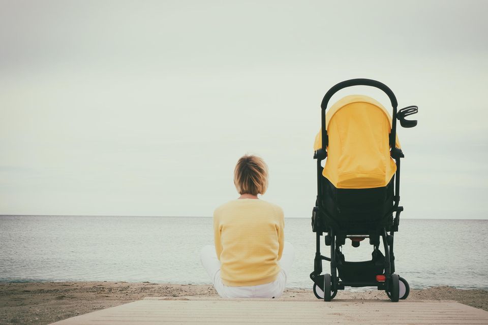 Mutter sitzt neben einem Kinderwagen und schaut aufs Meer