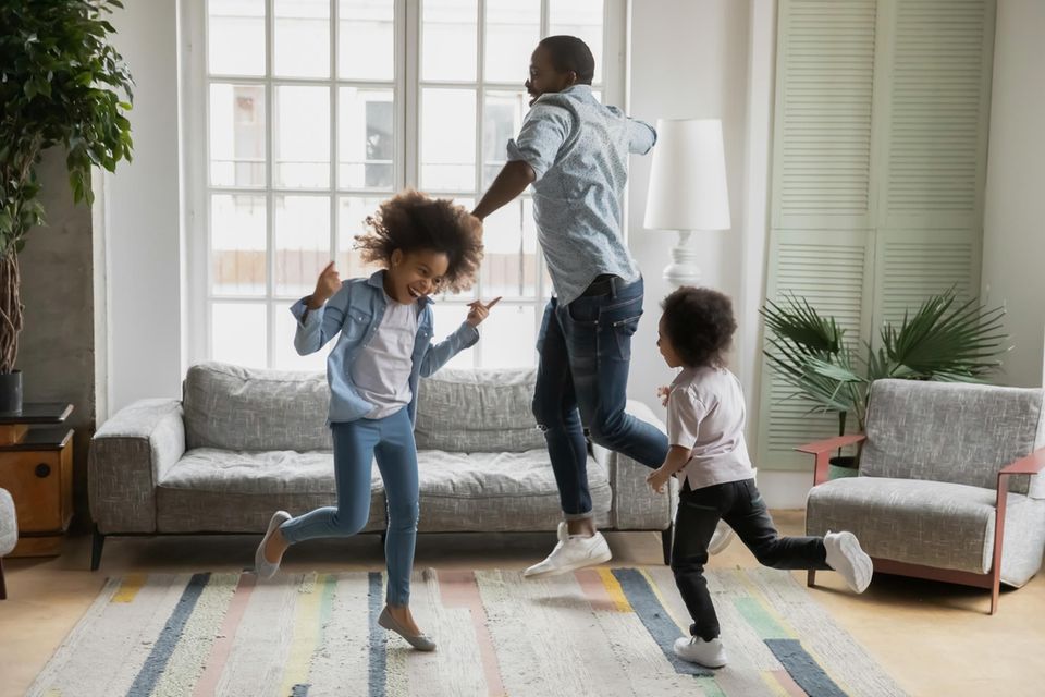 Vater und zwei Kinder tanzen durchs Wohnzimmer