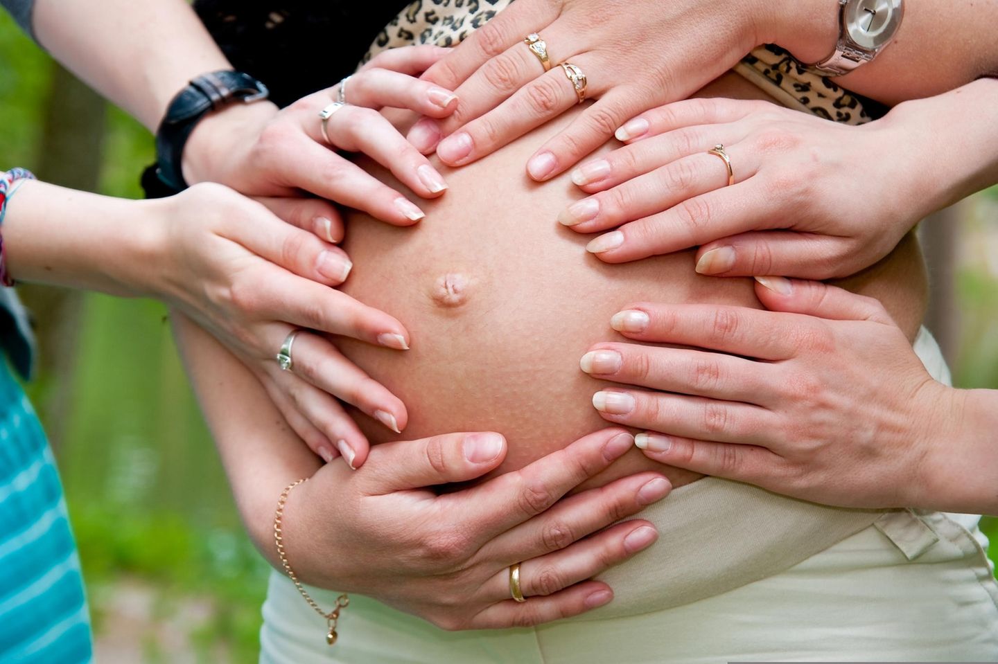 Viele Hände auf dem Babybauch einer Schwangeren