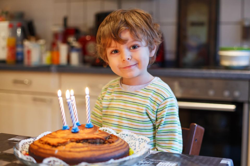 Kleiner Junge feiert seinen vierten Geburtstag mit einem Kuchen und Kerzen
