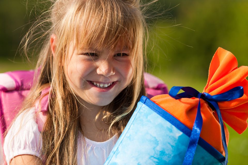 Geschenk zur Einschulung: Mädchen mit Schultüte und Schulranzen am ersten Schultag.