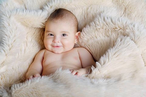 Makrosomie: Baby liegt lachend auf Fell
