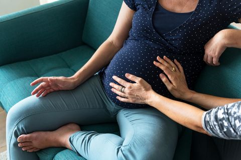 Nabelbruch: Schwangere sitzt auf dem Sofa, Hände tasten ihren bekleideten Bauch ab