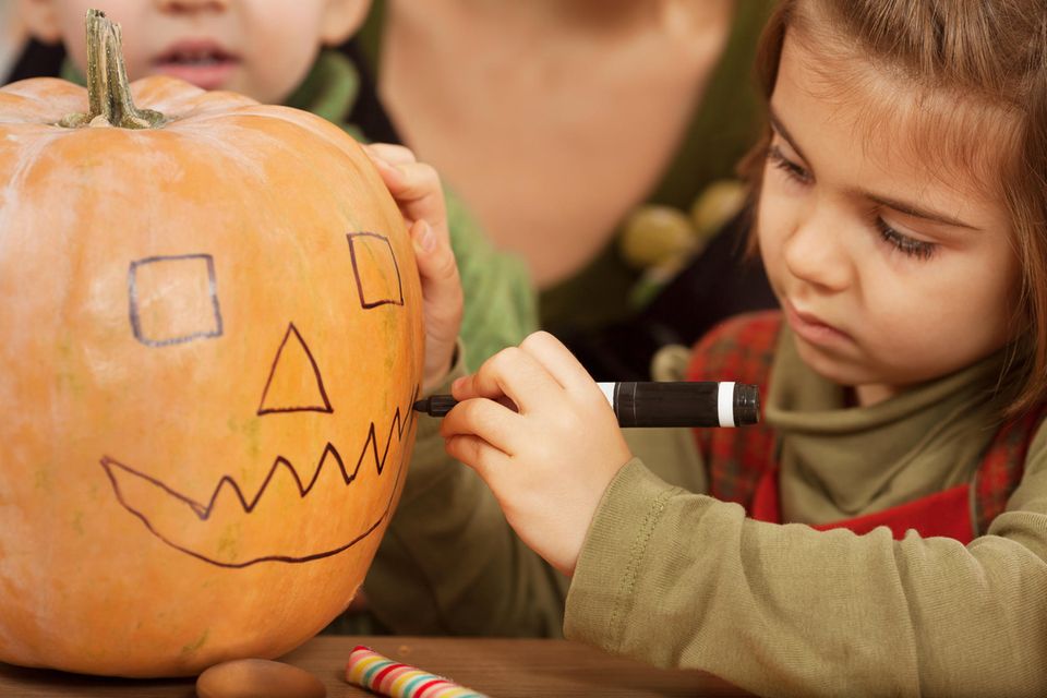 Kleines Mädchen zeichnet ein Gesicht auf ihren Halloween Kürbis