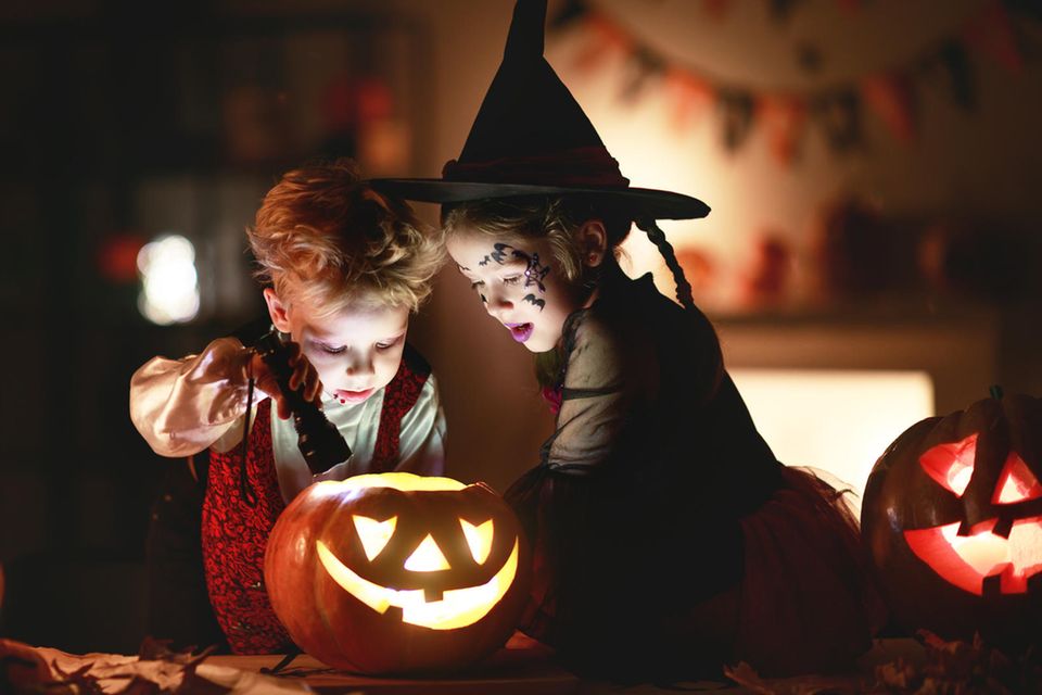 Zwei verkleidete Kinder im abgedunkelten Zimmer mit leuchtenden Halloween Kürbissen