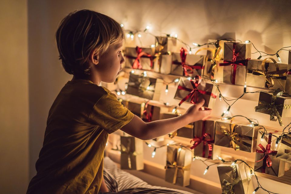 Junge mit Adventskalender-Geschenken und Lichterkette