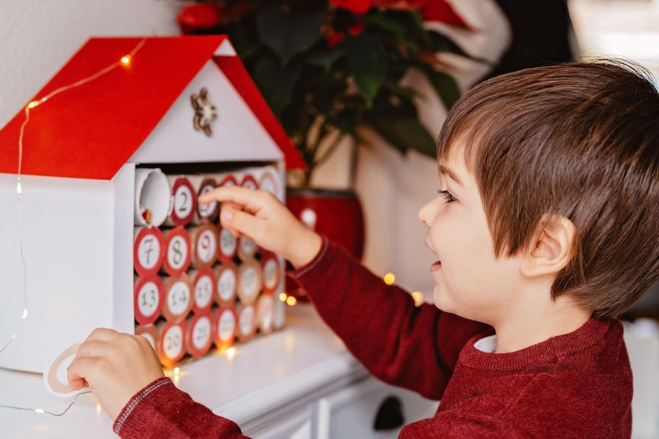 Kleiner Junge öffnet ein Türchen an seinem Adventskalender aus Klopapierrollen