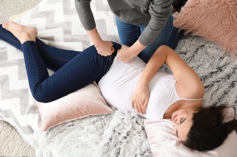 Eine Schwangere liegt von Kissen gestützt auf der Seite und wird massiert