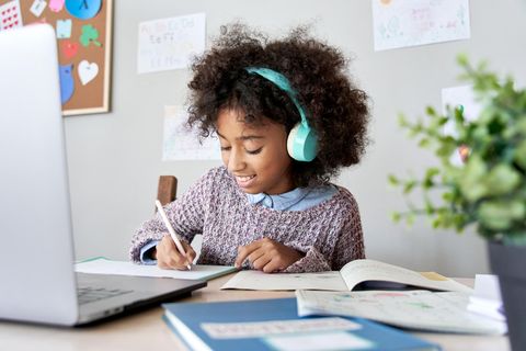 Kinderschreibtisch im Test: Lächelndes Mädchen mit  Kopfhörern macht Schulaufgaben am Tisch.