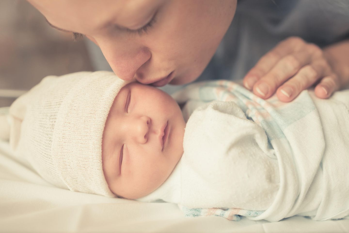 Geschenke zur Geburt: Frau küsst schlafendes Neugeborenes