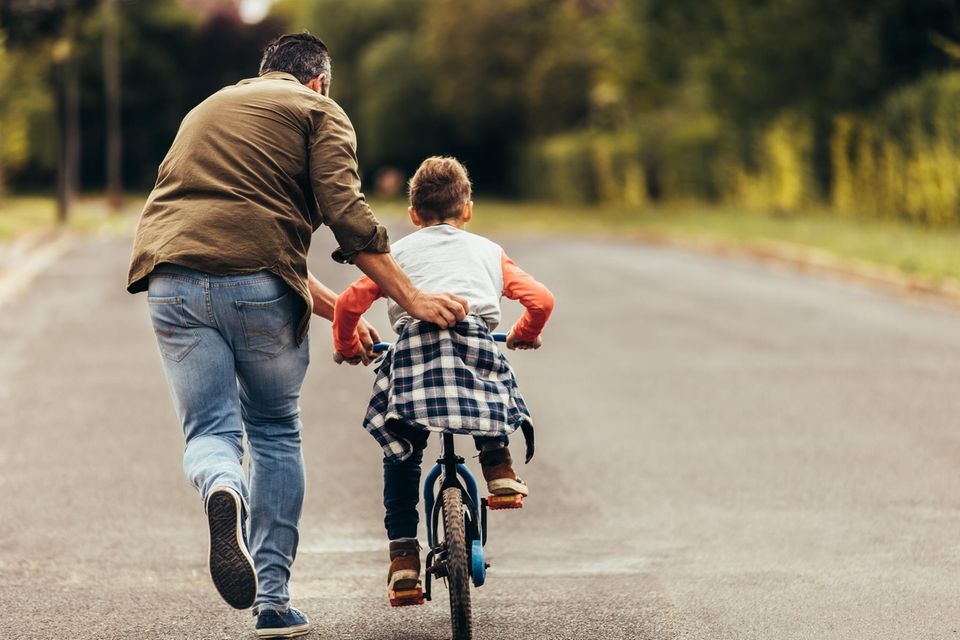 Erziehungsstil: Vater fährt mit Kind Rad