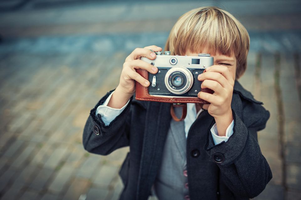 Kleiner blonder Junge steht draußen mit einem alten Fotoapparat in den Händen