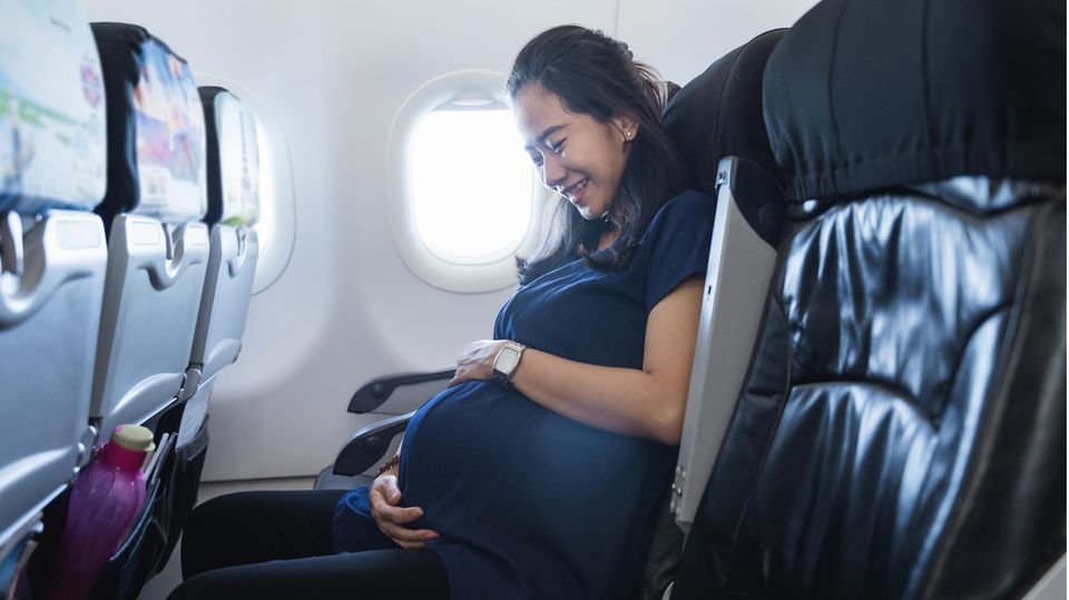 Ein schwangere sitzt im Flugzeug und hält ihren Bauch.