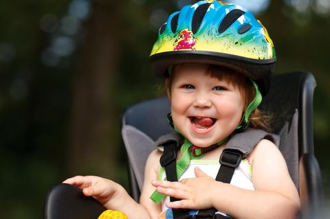 Kinderfahrradhelm im Test: Kleines fröhliches Mädchen mit buntem Helm auf Fahrradsitz.