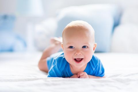 Ein Baby liegt auf dem Bauch und lacht in die Kamera